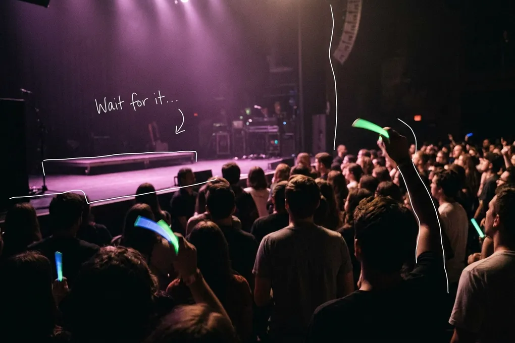 AI-generated image of a dark concert hall crowd seen from behind, with a few glow sticks raised toward a purple-lit stage. A white line traces the stage edge next to a handwritten note reading 'Wait for it'.