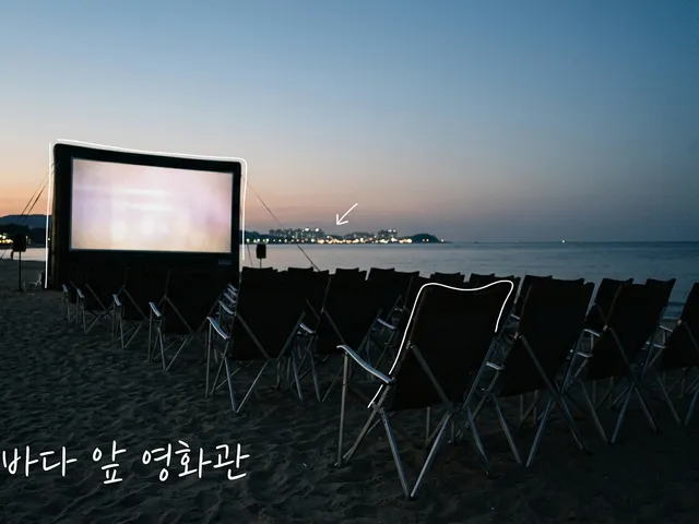 해 질 녘 바닷가 모래사장에 놓인 빈 접이식 의자들과 불이 켜진 야외 영화 스크린, 멀리 도시 불빛을 담은 AI 생성 이미지. 흰 선과 ‘바다 앞 영화관’ 손글씨가 얹혀 있다.