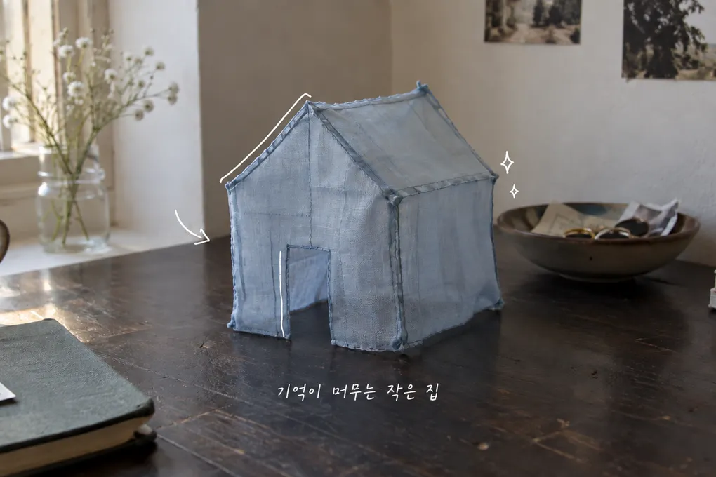 나무 탁자 위 작은 파란 천 집과 얇은 흰 선, 기억에 대한 손글씨를 담은 AI 생성 정물 이미지.
