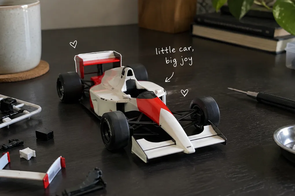 AI-generated model racing car and small assembly tools on a desk, with a white handwritten note.