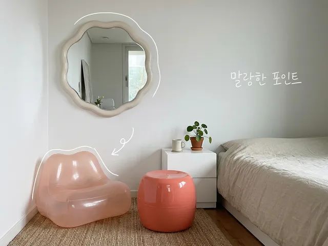 흰 벽 방 한구석에 물결 모양 거울, 반투명 분홍 의자, 코랄색 스툴이 놓인 AI 생성 이미지. 거울과 의자에 흰 선이 얹혀 있고 '말랑한 포인트' 손글씨가 있다.