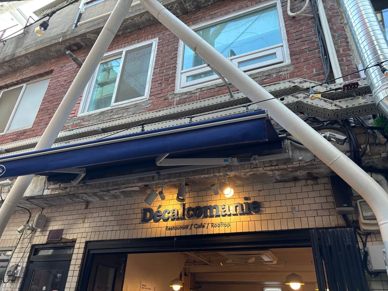 The storefront sign reading 'Décalcomanie Restaurant / Cafe / Rooftop' on a white tiled wall under a blue awning