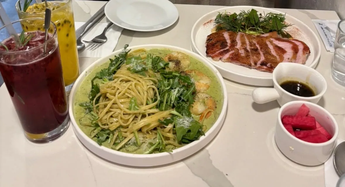 A table with green-sauce pasta, grilled steak slices and two fruit drinks