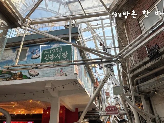 해방촌 신흥시장 골목의 투명한 지붕 아래 ‘Since 1953 신흥시장’ 벽화 간판을 직접 찍은 사진. 간판을 따라 흰 손그림 선이 그어져 있고 ‘해방촌 한 바퀴’ 손글씨가 있다.
