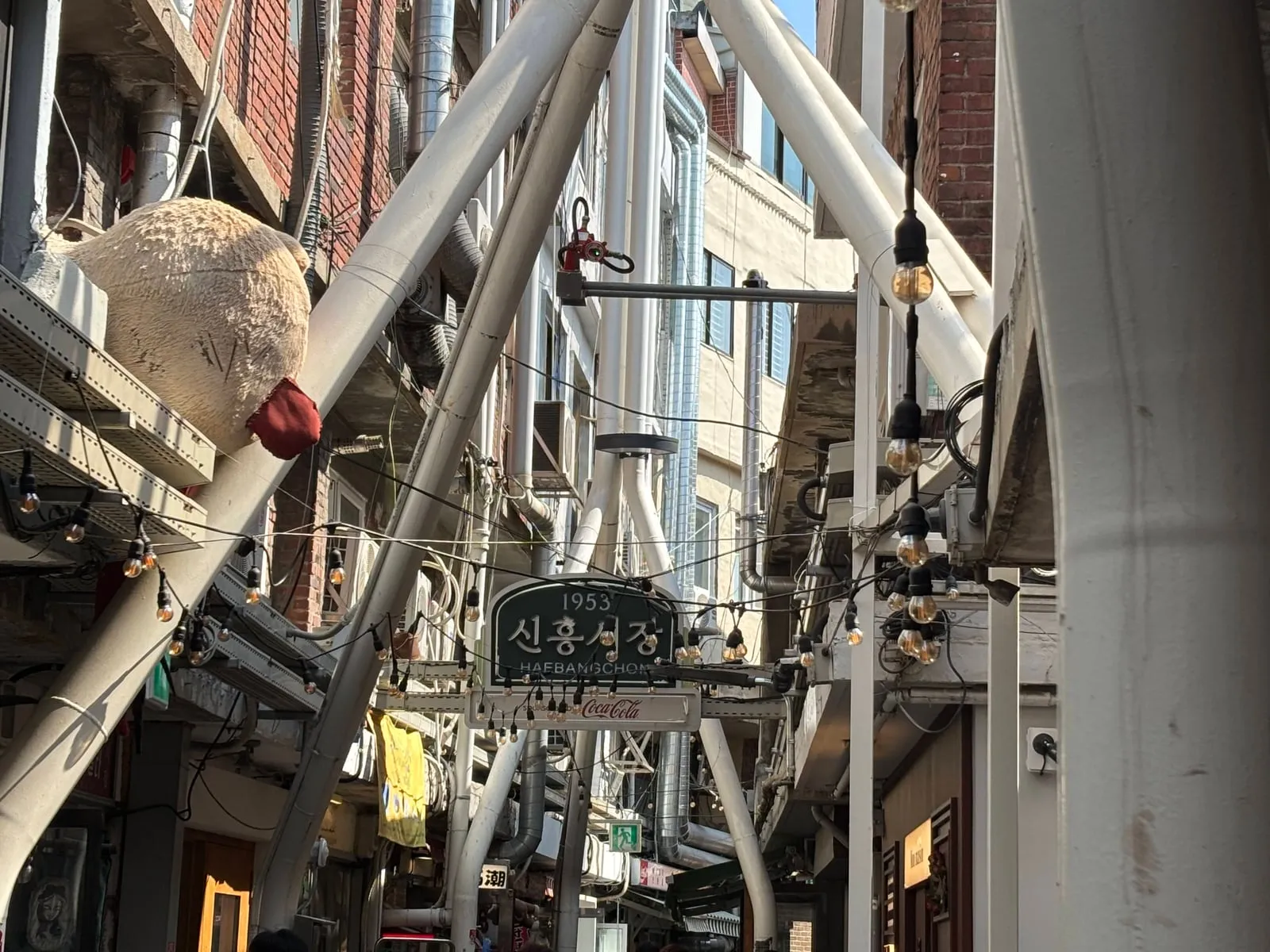 White pipes and string lights running over the market alley, with shop signs