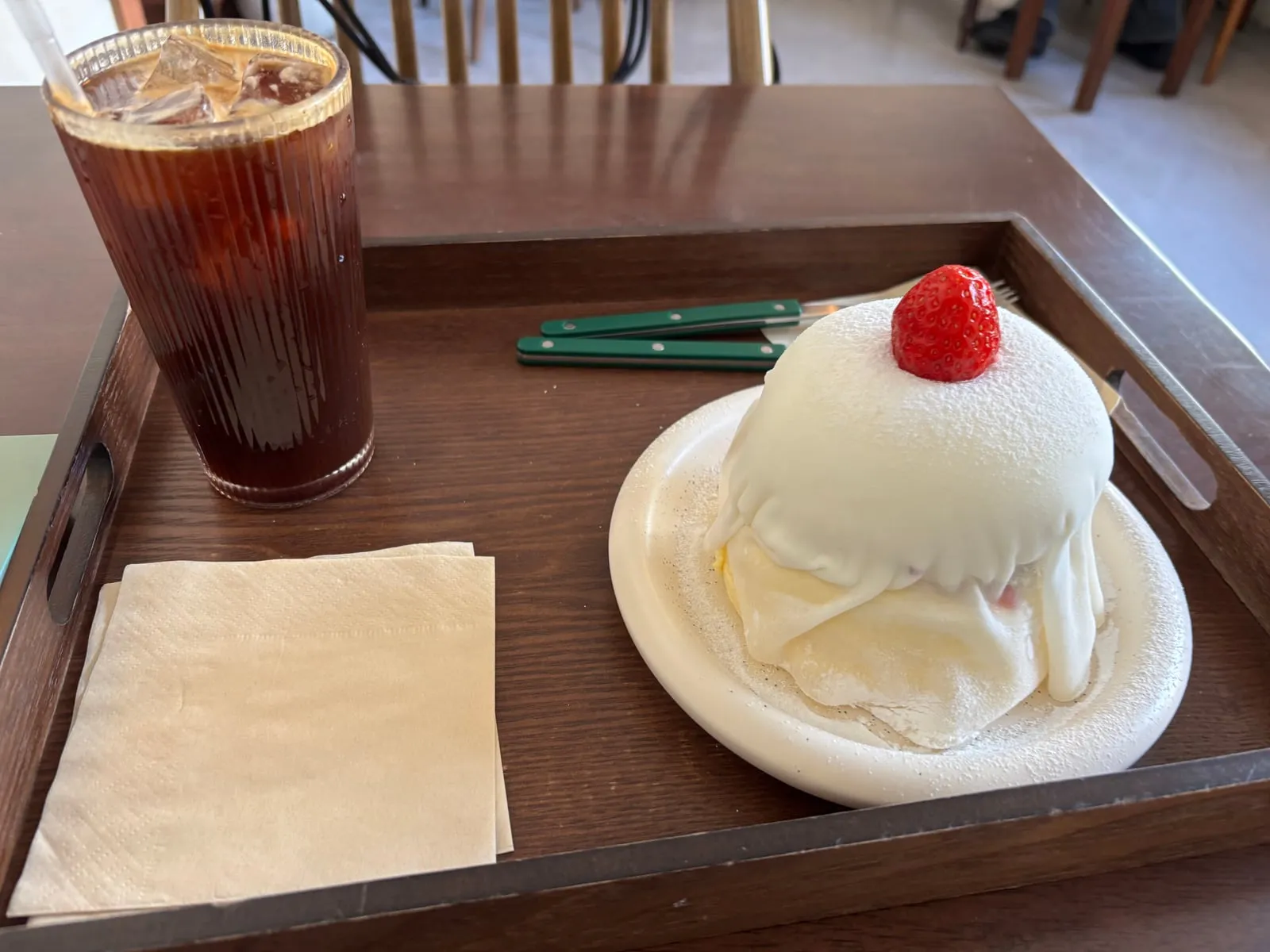 A white mochi pancake topped with a strawberry and an iced coffee on a wooden tray