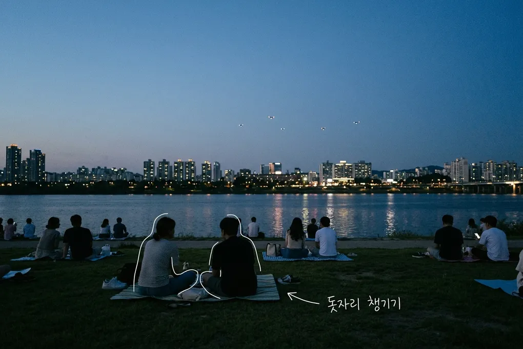 해 질 녘 한강 잔디밭에서 돗자리에 앉은 사람들이 강 건너 야경과 하늘의 작은 드론 불빛을 바라보는 AI 생성 이미지. 흰 선과 ‘돗자리 챙기기’ 손글씨가 얹혀 있다.