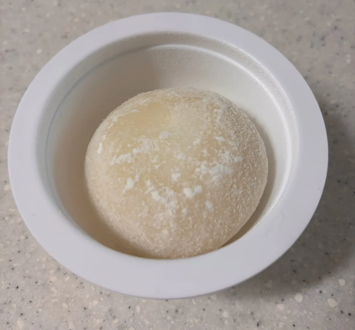 A single round rice cake lightly dusted with white powder inside a white cup
