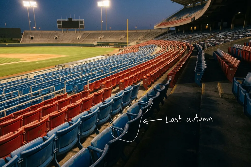 AI-generated dusk view of empty blue and red seats in a baseball stadium under floodlights, with a thin white line around a row of seats and a handwritten note reading 'Last autumn'.