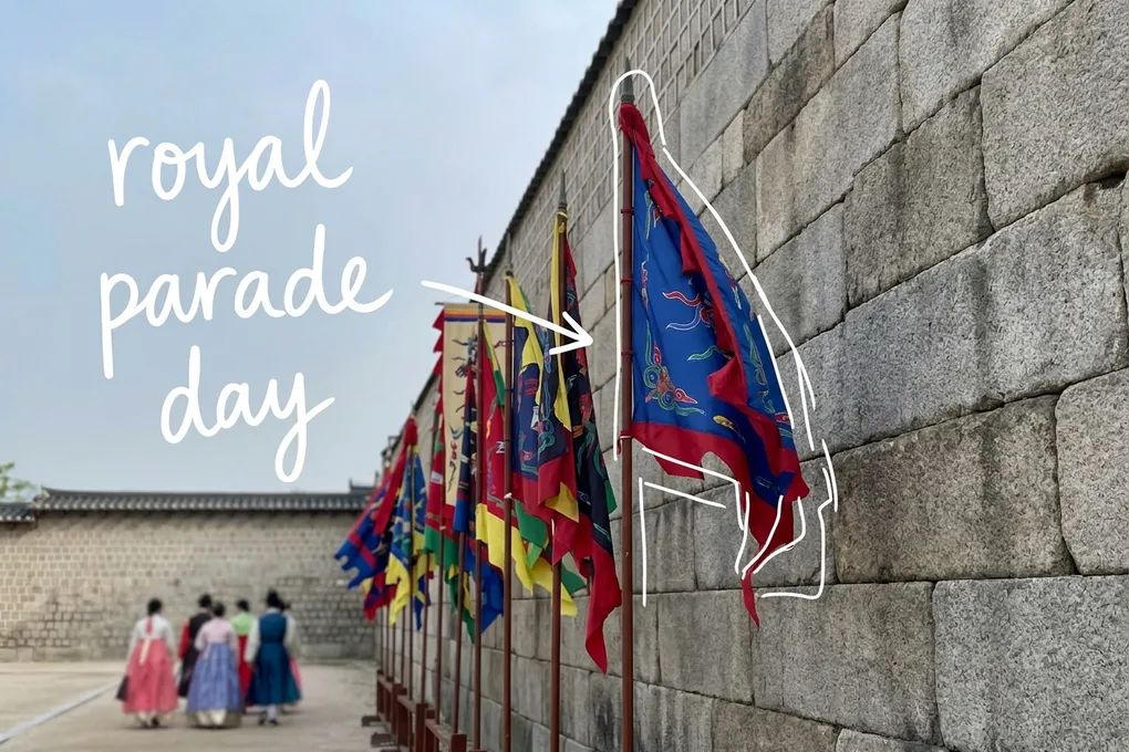 AI-generated view of colorful traditional banners along an old palace stone wall, with people in hanbok walking far ahead, thin white lines and the handwritten note 'royal parade day'.