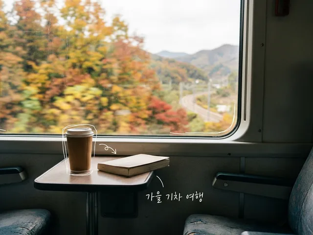 기차 창가 접이식 테이블 위의 종이컵과 책, 창밖으로 지나가는 노랗고 붉은 단풍을 담은 AI 생성 이미지. 흰 선과 ‘가을 기차 여행’ 손글씨가 얹혀 있다.