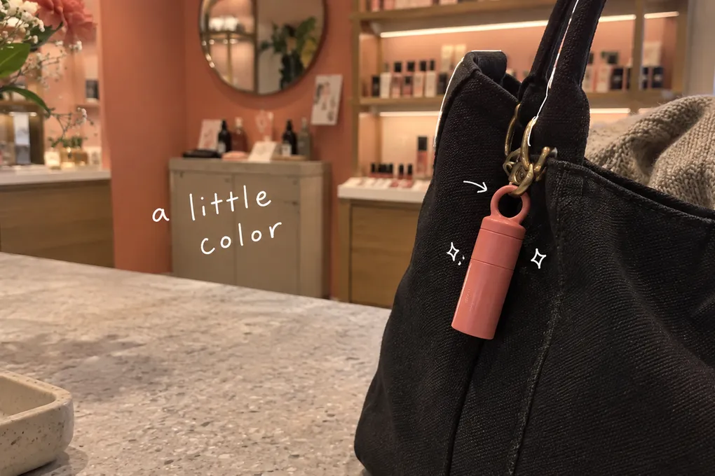 AI-generated illustration of a coral lip balm clipped to a black bag, with white pen marks and the handwritten words a little color.