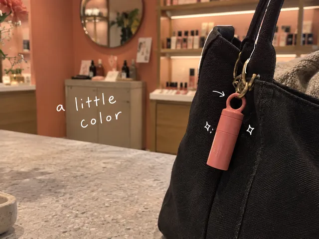 AI-generated illustration of a coral lip balm clipped to a black bag, with white pen marks and the handwritten words a little color.