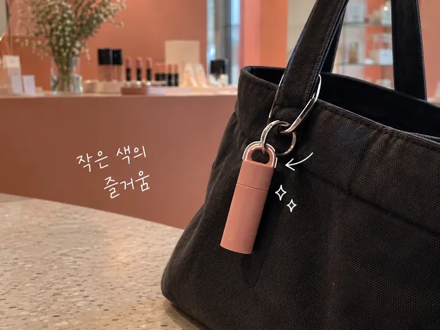 검은 가방에 매달린 코랄색 립밤과 흰 펜 선, 조금의 색이라는 손글씨를 담은 AI 생성 일러스트.