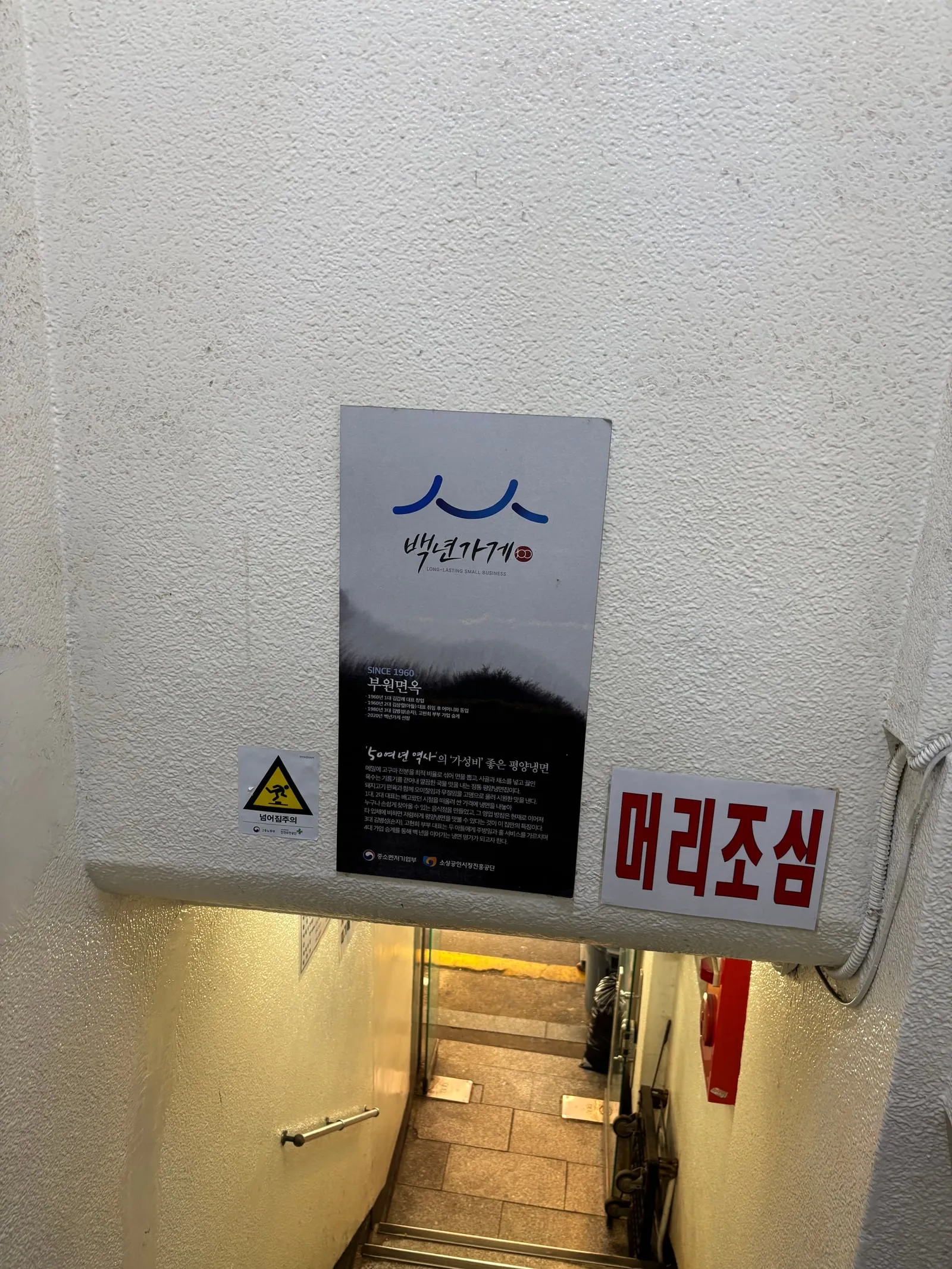 A 'Centennial Business Buwon Myeonok SINCE 1960' notice and a 'watch your head' sign at the stairway entrance