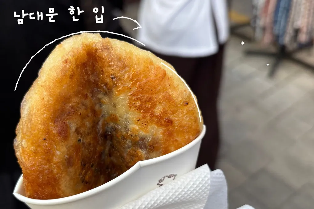 종이컵에 담긴 노릇하게 구운 호떡을 직접 찍은 사진. 호떡의 윤곽을 따라 흰 손그림 선이 그어져 있고 ‘남대문 한 입’ 손글씨가 있다.