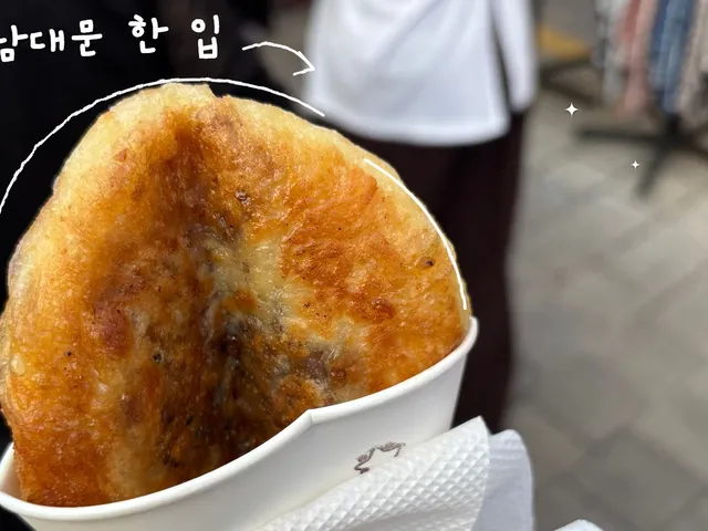 종이컵에 담긴 노릇하게 구운 호떡을 직접 찍은 사진. 호떡의 윤곽을 따라 흰 손그림 선이 그어져 있고 ‘남대문 한 입’ 손글씨가 있다.