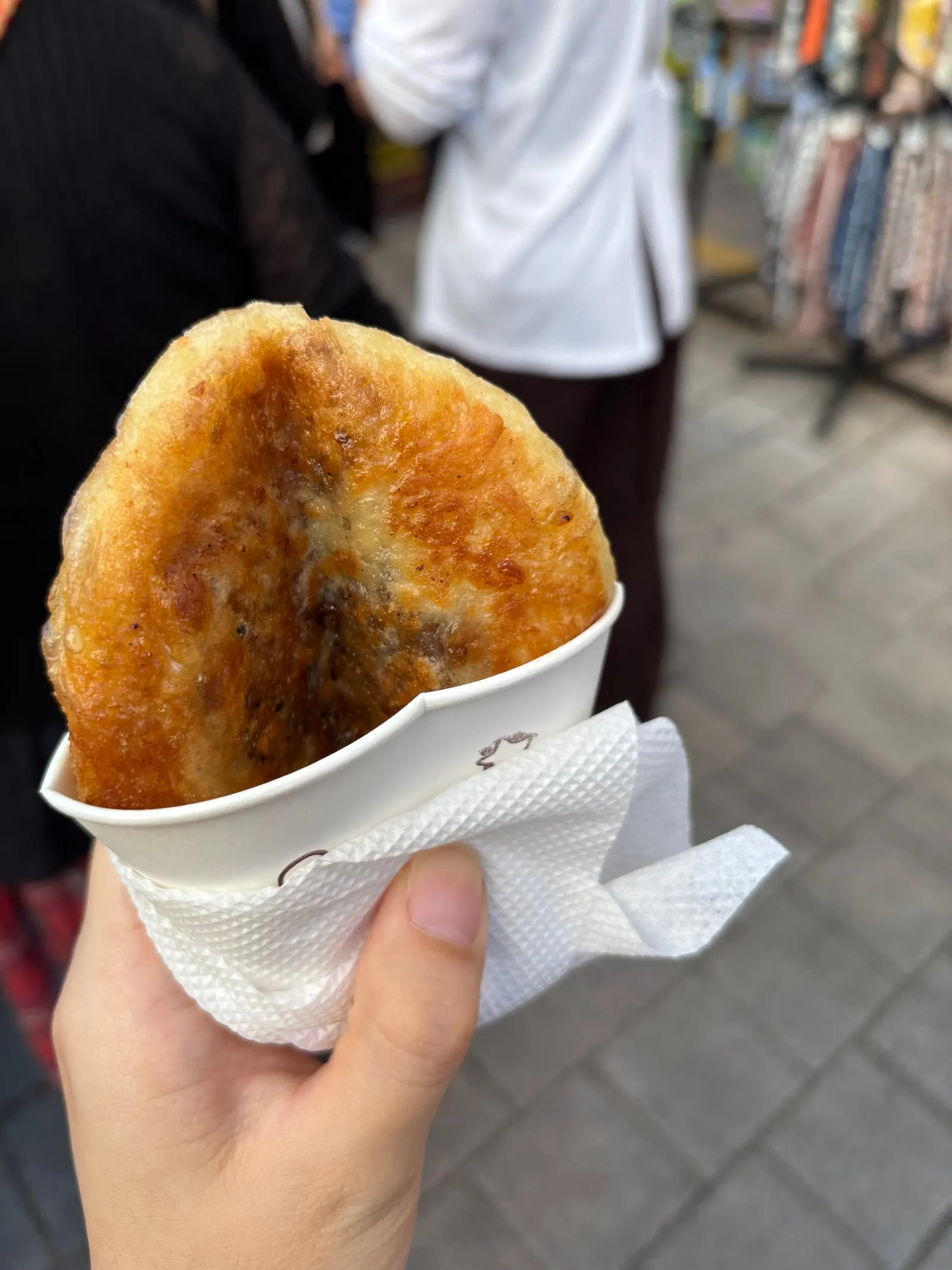 A hand holding a golden fried hotteok in a paper cup