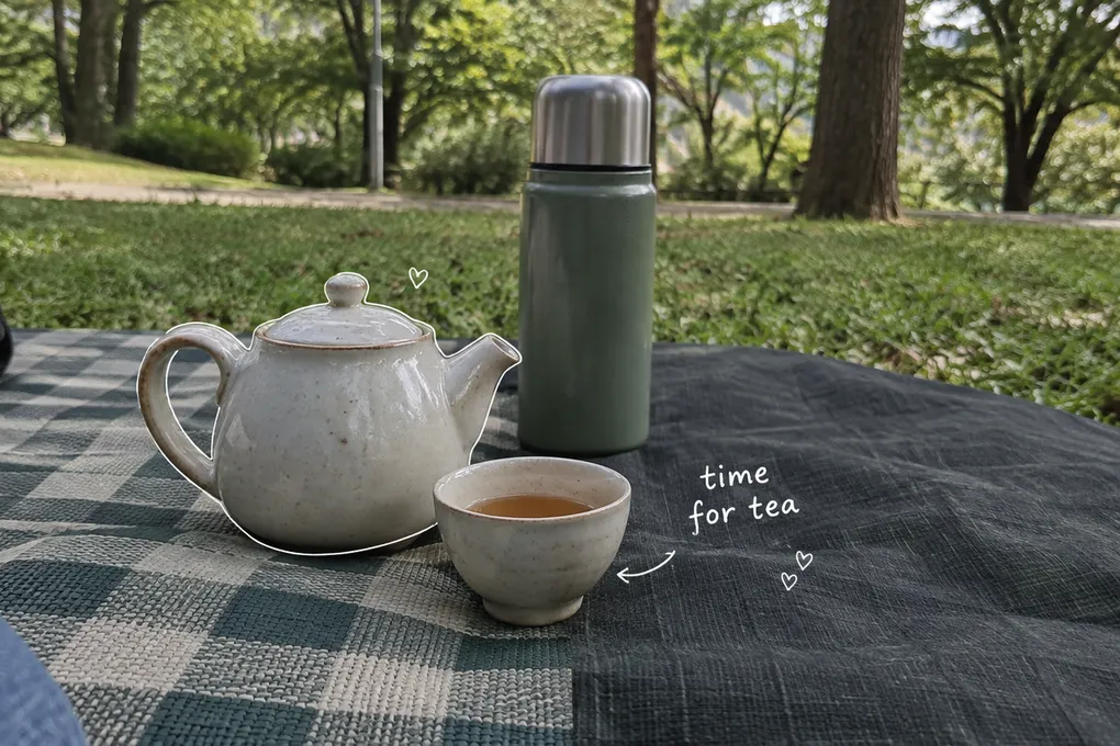 AI-generated small teapot, filled cup and thermos on a park picnic mat, with a white time-for-tea note.